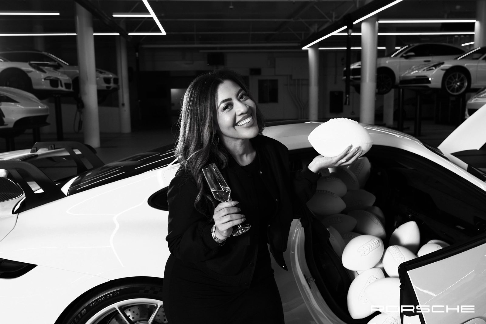 Alexandria Reed laughing, holding a football and a glass of champagne beside a white sports car
